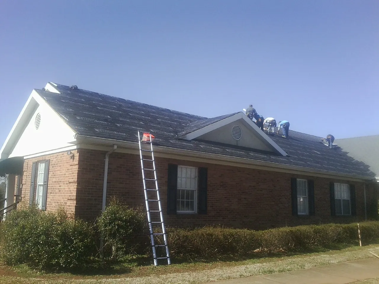Crew tearing shingles off a brick ranch roof with a ladder set — Emergency Roof Repair work by our crew in Wauseon