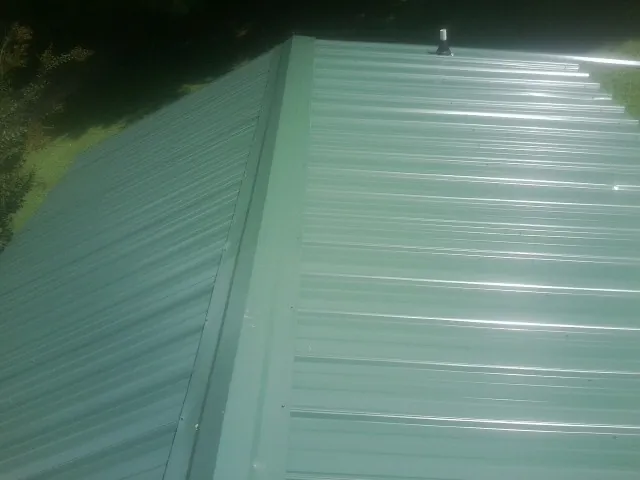 New green metal panels meeting at the ridge of a roof — Flat Roof Repair work by our crew in Wauseon