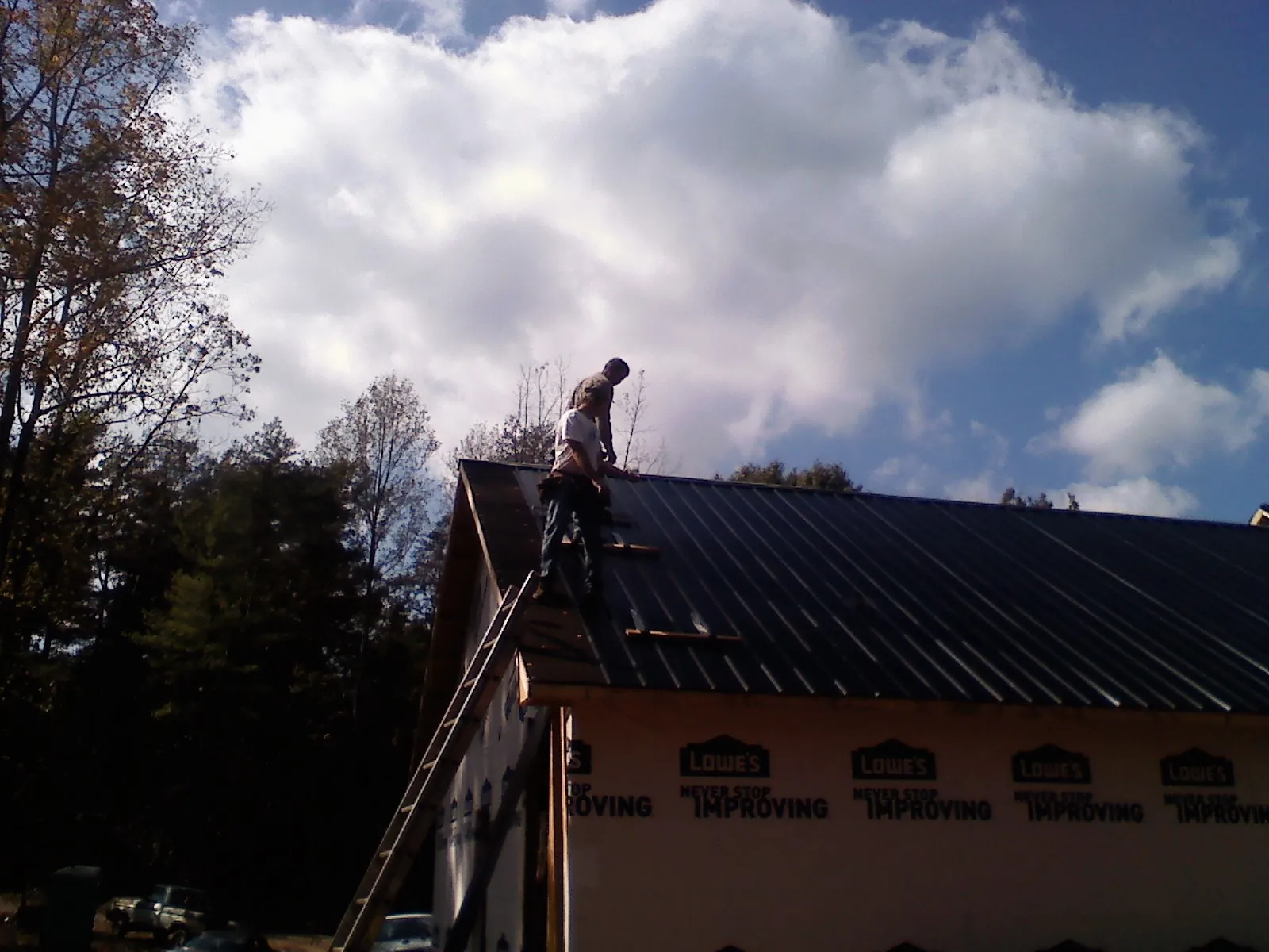 Roofer fastening dark metal panels high against a cloudy sky, from a Roof Inspection job in Wauseon