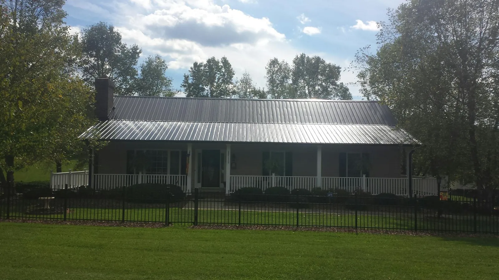 Gray metal roof on a brick ranch with a full width front porch — Gutter Guard Installation work by our crew in Wauseon