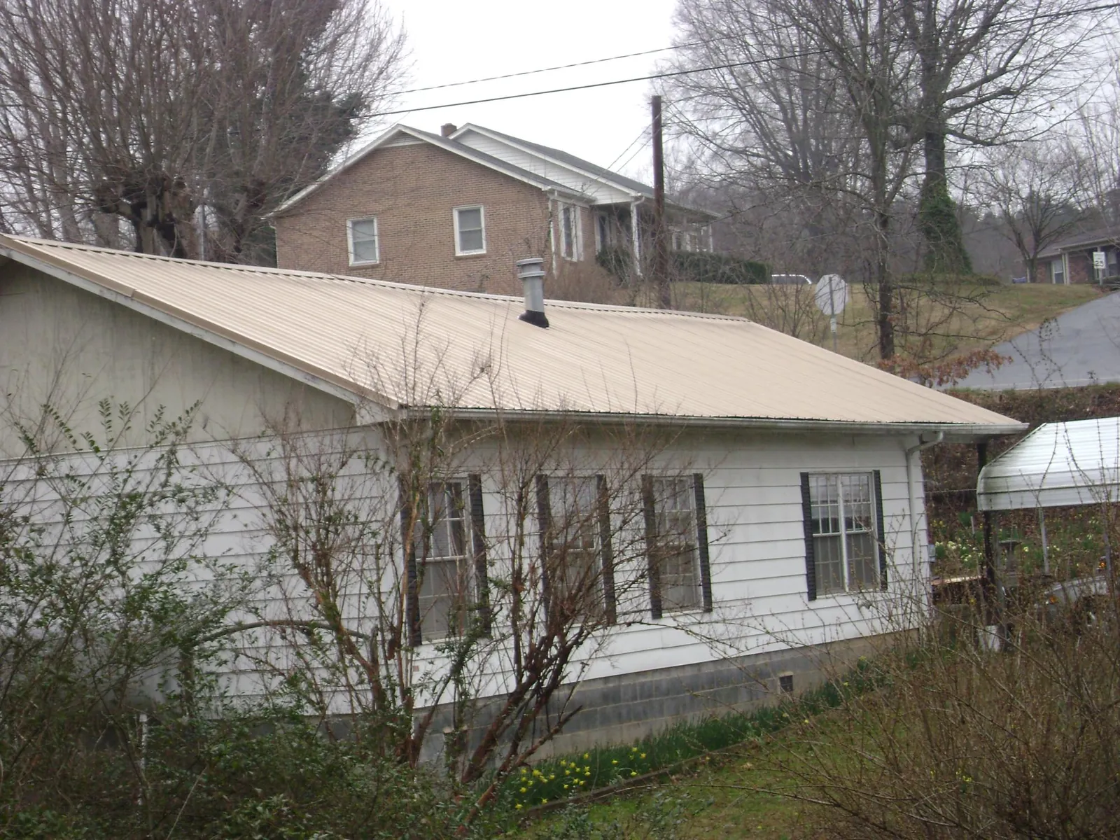 Tan metal roof on a white sided house set into a hillside — Commercial Roofing by Roofing Brothers in Wauseon