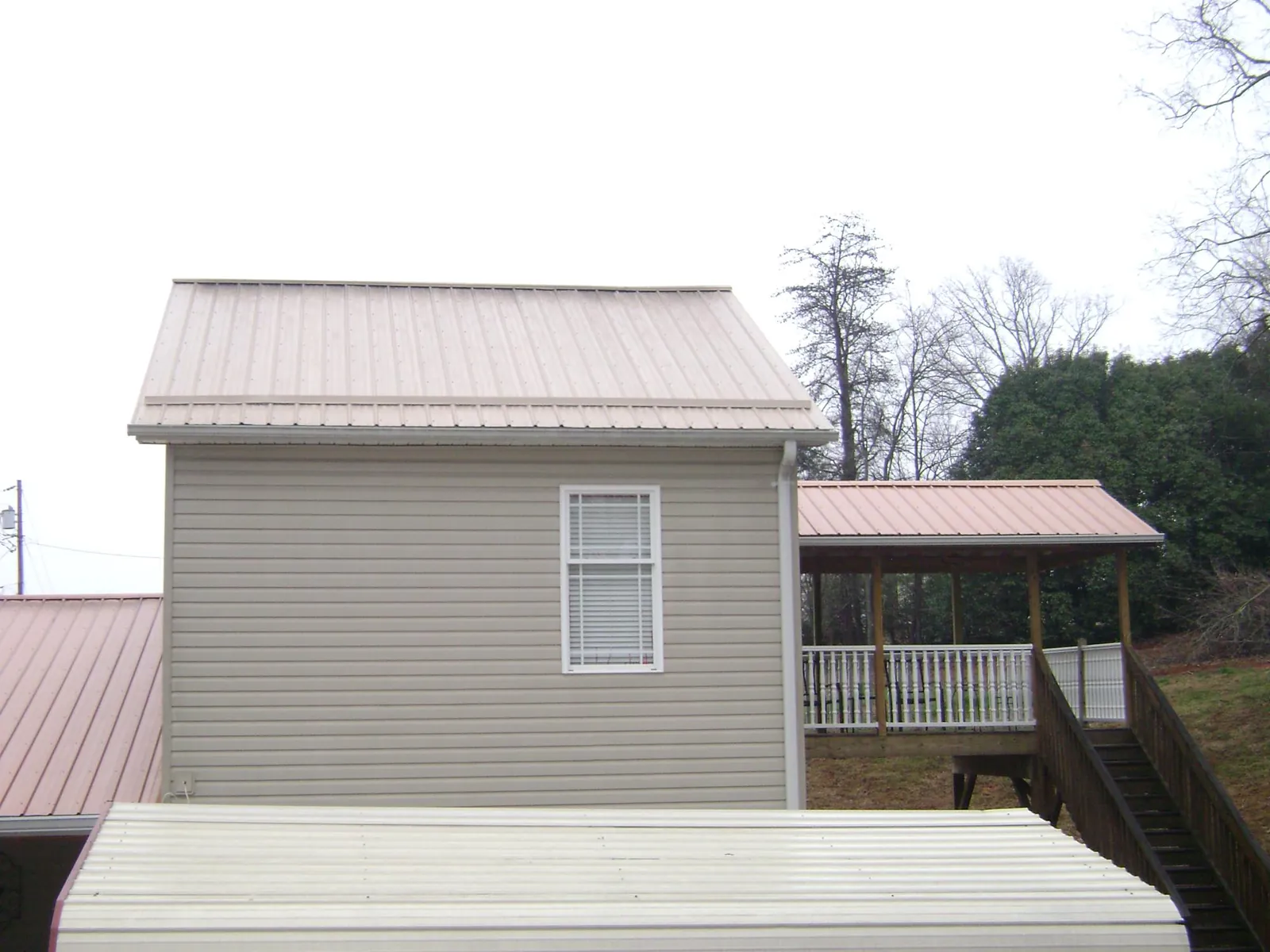 Tan metal roofs on a two story addition and attached porch, from a Roof Replacement job in Wauseon